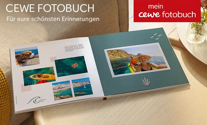 Geöffnetes Fotobuch mit Urlaubsfotos am Meer und maritimen Design, platziert auf einem Holztisch.