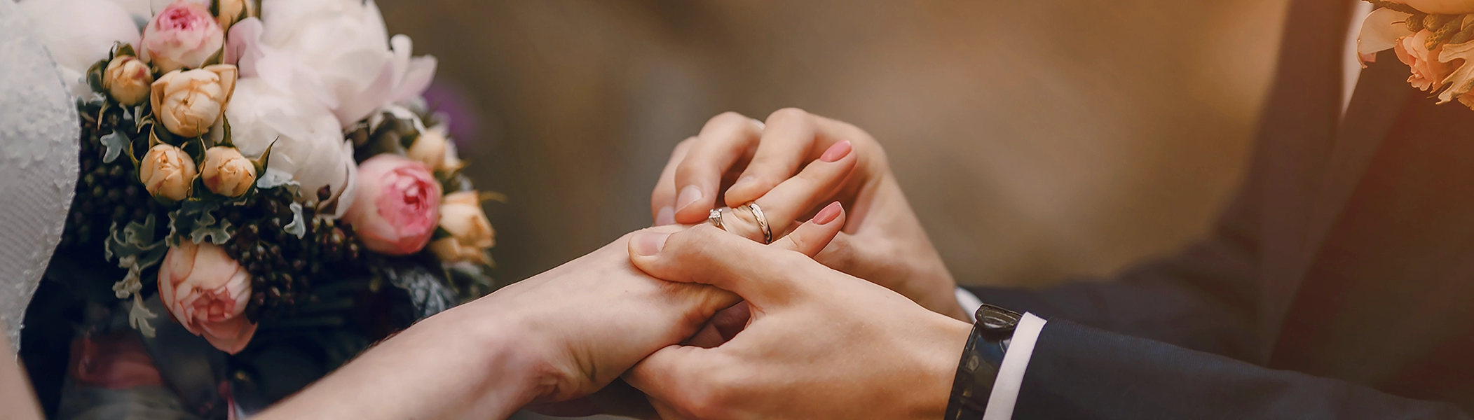 Brautstrauß und Hände eines Paares beim Anstecken des Rings. Entdeckt Geschenkideen zur Hochzeit in der ROSSMANN Fotowelt!