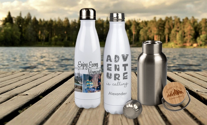 Weiße Thermosflaschen mit Foto und Text oder Gravur, stehen zusammen mit einer kleinen Edelstahlflasche mit graviertem Bambusdeckel auf einem Holzsteg vor einem See