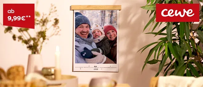 Ein Kalender mit winterlichem Foto hängt an einer Wand, umgeben von natürlicher Dekoration.