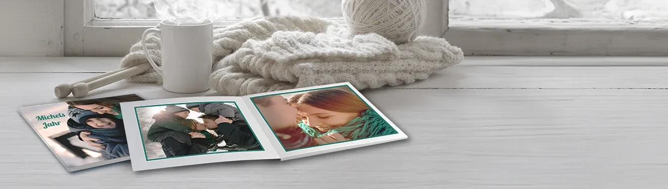 Ein aufgeschlagenes Fotobuch mit fröhlichen Momentaufnahmen. Haltet eure schönsten Fotos in einem Fotobuch fest.