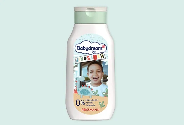 Weiße Babydream Bad & Shampoo Flasche mit grünem Deckel, Kinderfoto und niedlichem Dinosauriermotiv auf der Vorderseite.