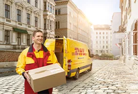 DHL-Lieferfahrer in uniformiertem Gelb-Rot-Outfit trägt Paket aus einem geöffneten Lieferwagen in städtischer Umgebung.