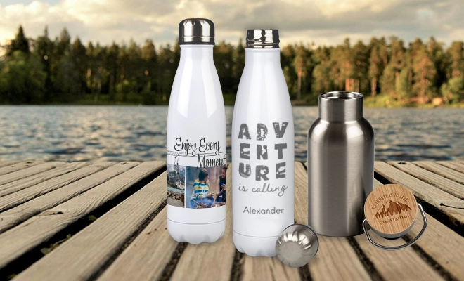 Weiße Thermosflaschen mit Foto und Text oder Gravur, stehen zusammen mit einer kleinen Edelstahlflasche mit graviertem Bambusdeckel auf einem Holzsteg vor einem See
