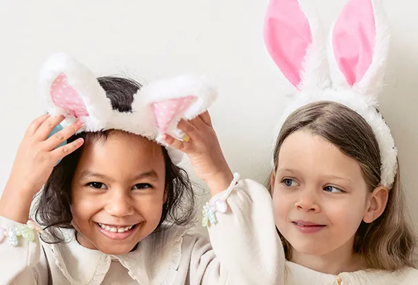 Zwei Kinder mit Hasenohren-Stirnbändern lachen fröhlich. Entdeckt unsere Fotogeschenke-Ideen zu Ostern für die ganze Familie!