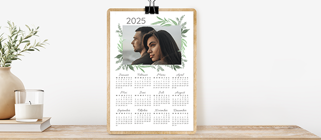 Ein Kalender für das Jahr 2025 mit einem Foto von zwei Personen und dekorativen Blattmotiven.