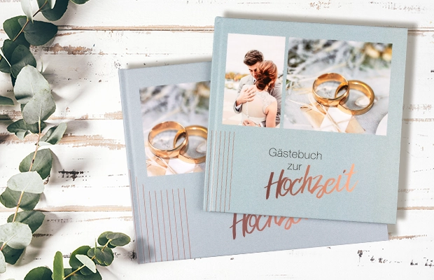 Gästebuch mit Brautpaar-Fotos und goldenen Ringen auf Holzhintergrund mit Zweigen als wertvolles Fotogeschenk zur Hochzeit.