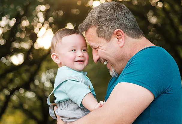 Ein lächelnder Papa mit Baby – ein Motiv aus der Babywelt, in der ihr personalisierte Geschenke zur Geburt entdecken könnt.