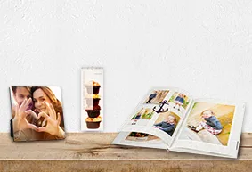Verschiedene personalisierte Fotoprodukte wie ein Fotoaufsteller, ein Terminkalender und ein Fotobuch auf einem Holztisch.