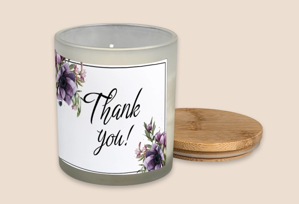 Duftkerze mit Deckel als Geschenkidee zur Hochzeit und Aufschrift ‚Thank you!‘, umgeben von lila Blumen auf weißem Etikett.