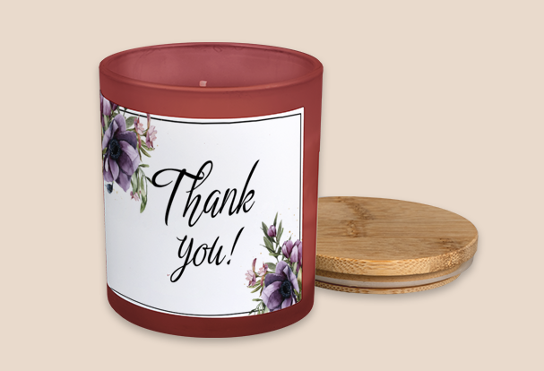 Duftkerze mit Deckel als Geschenkidee zur Hochzeit und Aufschrift ‚Thank you!‘, umgeben von lila Blumen auf weißem Etikett.