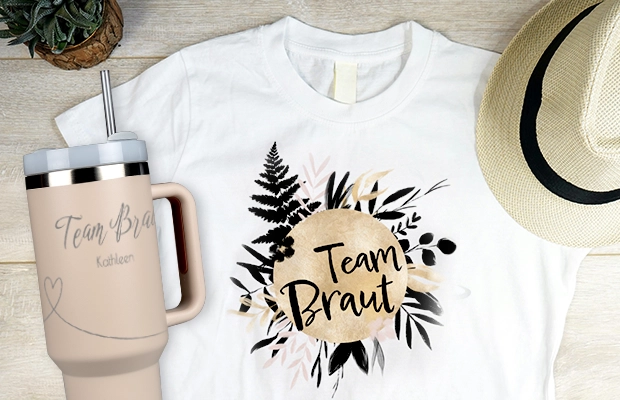 Weißes T-Shirt mit Desing und Schriftzug 'Team Braut', daneben Thermobecher mit Text 'Team Braut Kathleen' als stylishe Fotogeschenke Hochzeit.