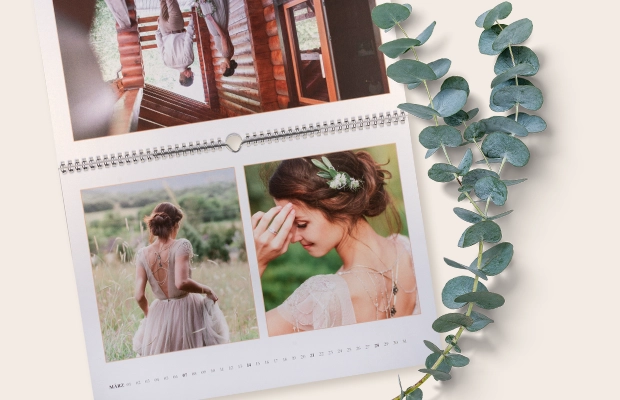 Aufgeschlagener Kalender mit Brautfotos neben einem Zweig als stilvolles, personalisiertes Hochzeitsgeschenk für 12 besondere Monate.