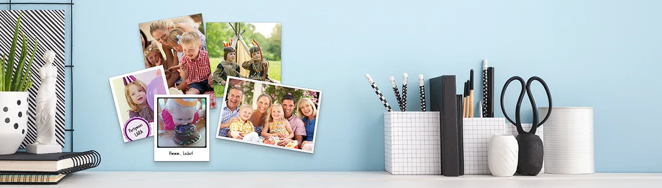 Mehrere Fotoabzüge mit Familien- und Kinderfotos als persönliche Wanddekoration an einer hellblauen Wand arrangiert