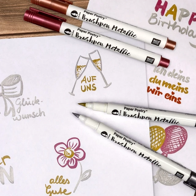 Brushpens in Metallicfarben und kreative Zeichnungen wie Blumen, Herzen und Text auf Papier.