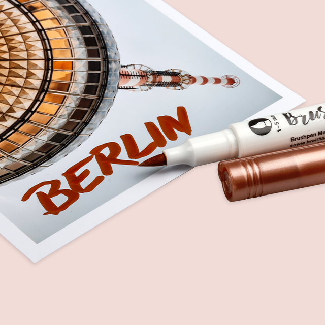 Ein Brushpen in metallischen Roségold, mit dem das Wort „Berlin“ mit einem Herz auf ein Foto geschrieben wird.